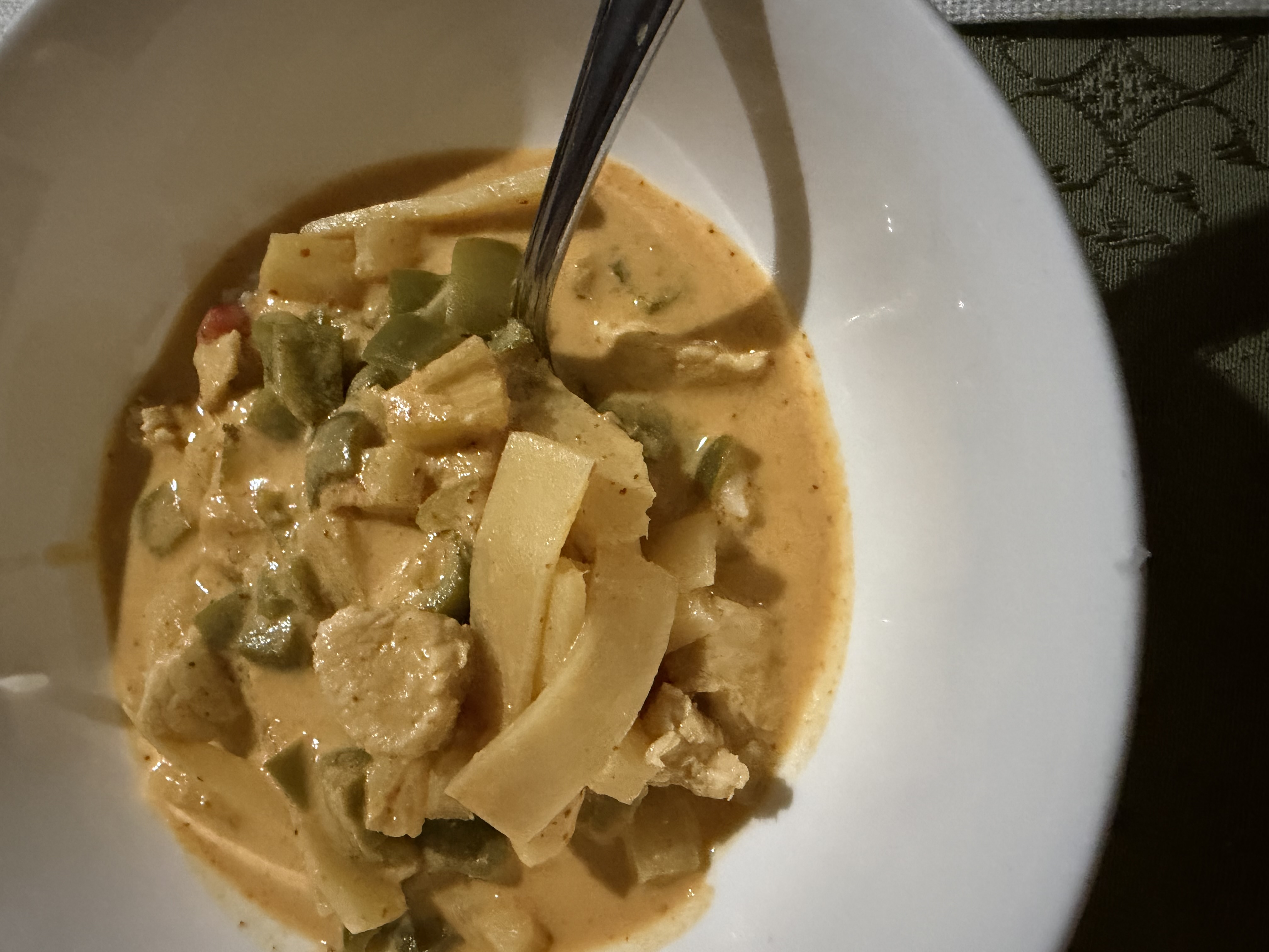 A white bowl of creamy red Thai curry with chicken, green bell peppers, and bamboo shoots, with a spoon