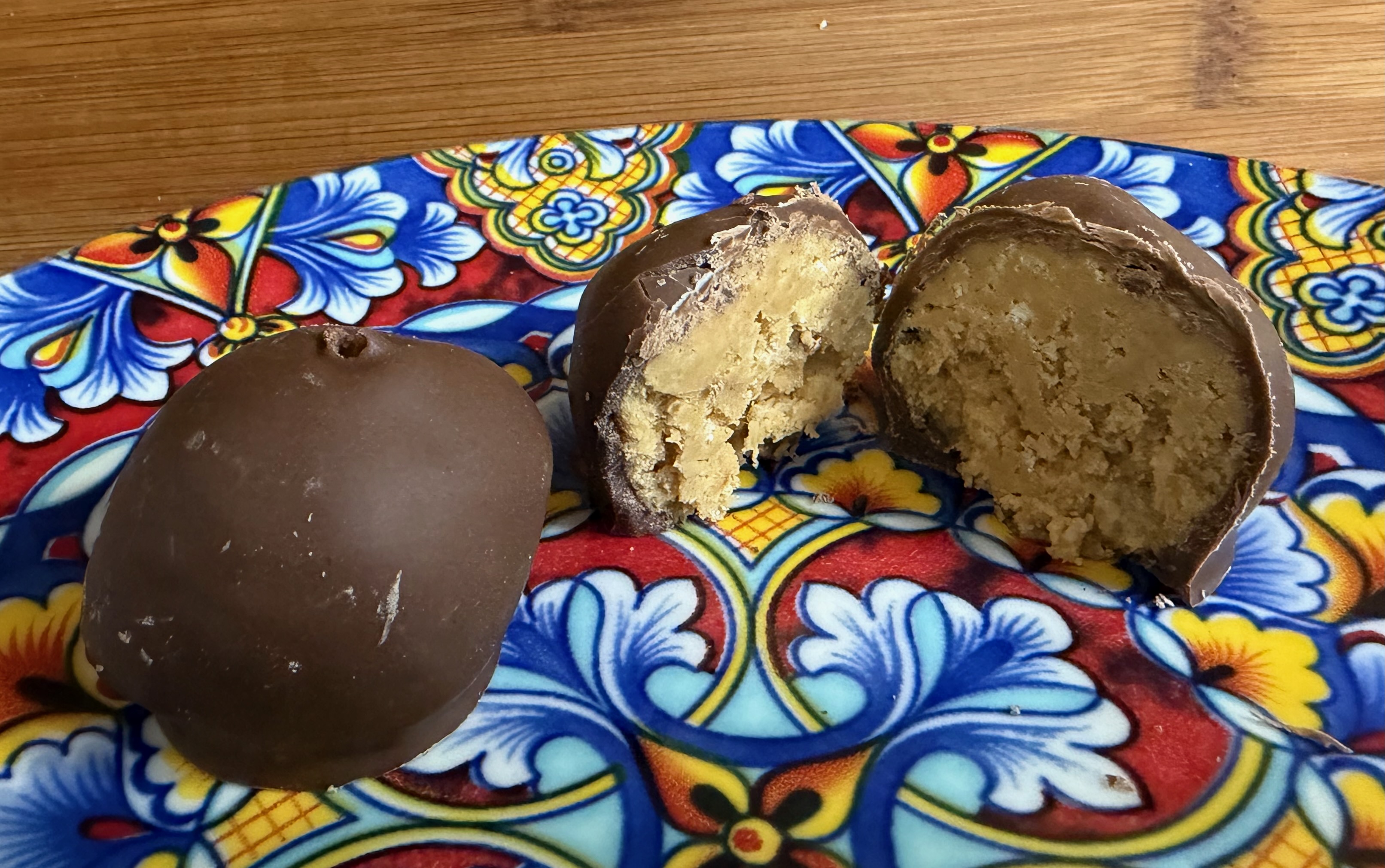 Three chocolate-coated peanut butter balls on a colorful plate, two broken open to show the creamy peanut butter and Rice Krispie center